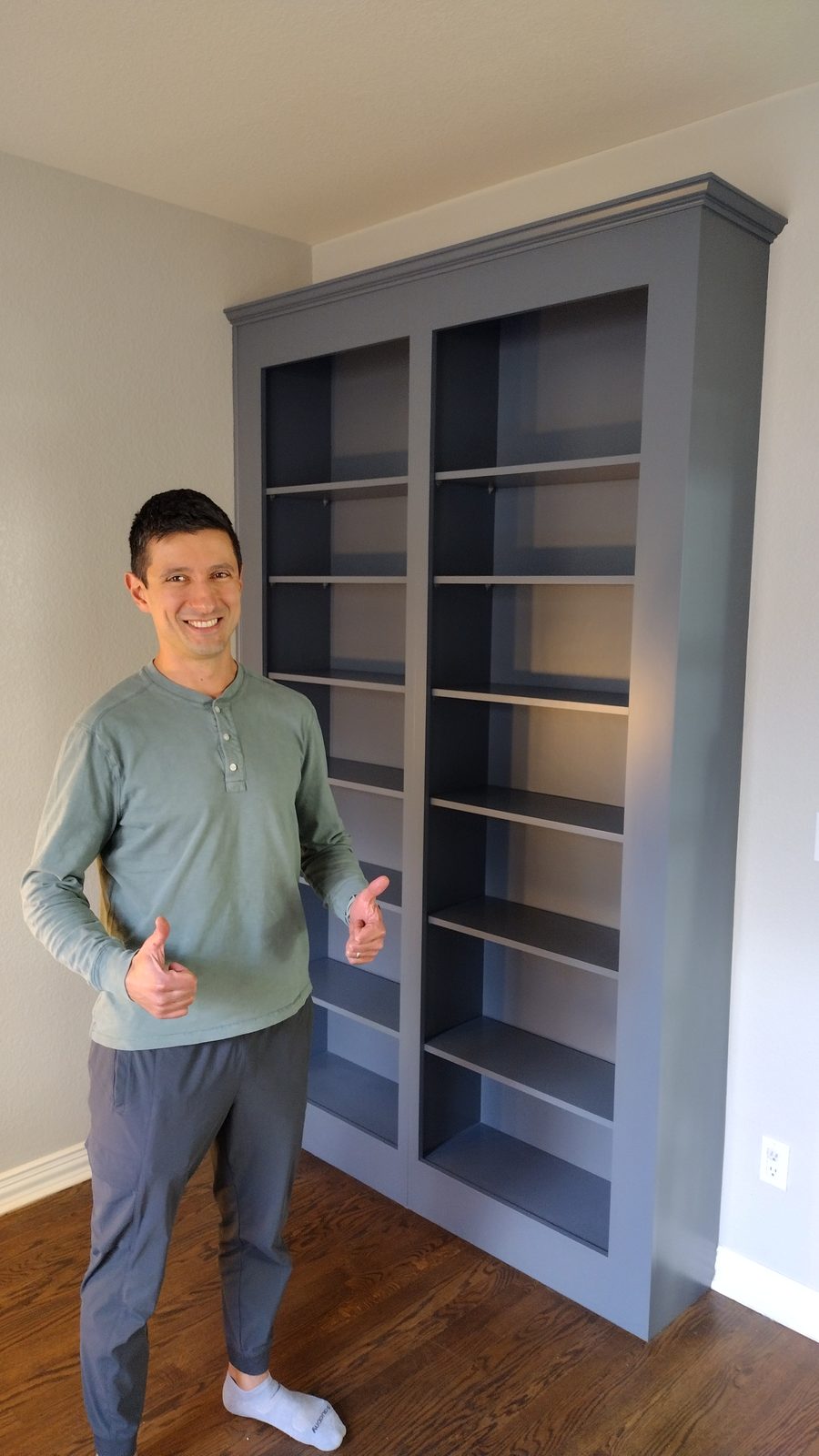 Homeowner giving two thumbs-up beside his newly painted gray built-in bookcase