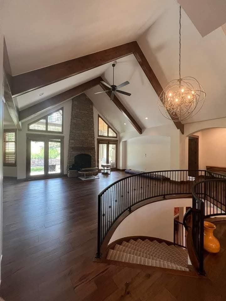 Finished great room with wood beams, stone fireplace and iron stair railing by Rock's Finest Finishes